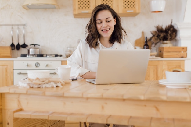 La donna caucasica millenaria felice si siede al tavolo lavora online sul computer portatile consulta il cliente sul web giovane studentessa sorridente studia lontano sul concetto di elearning del computer