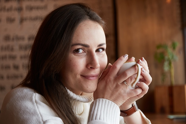 La donna caucasica rilassata beve tè o caffè