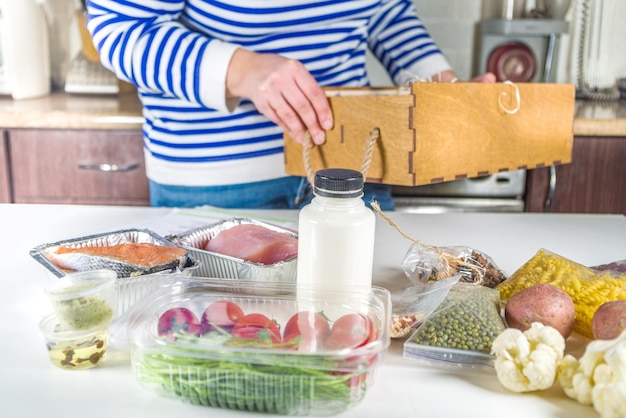 La donna caucasica smonta la scatola con la consegna degli ingredienti, ricette. Concetto di consegna del kit pasto. Impostare vari cibi sani con ricette per cucinare. Ordinazione online della consegna di generi alimentari dello chef del ristorante