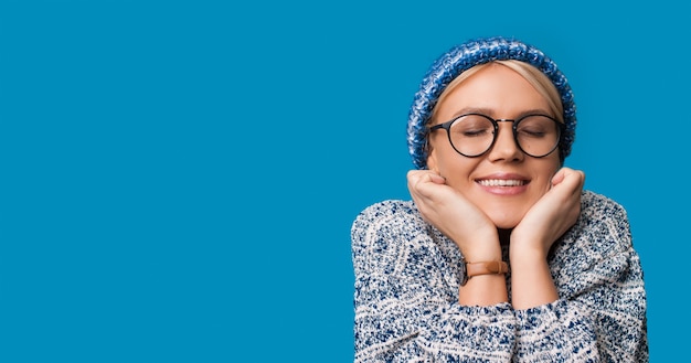 La donna caucasica sta sognando qualcosa in posa con un cappello caldo su una parete blu con spazio libero