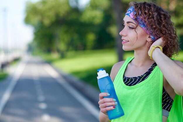 La donna che corre sta facendo una pausa nell'acqua potabile durante la corsa nel parco estivo