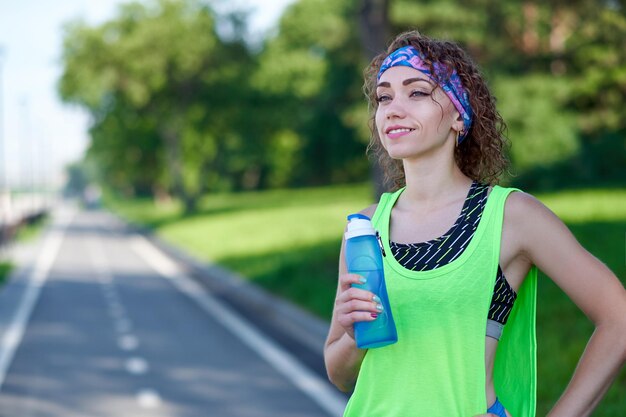 La donna che corre sta facendo una pausa nell'acqua potabile durante la corsa nel parco estivo