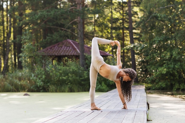 La donna che fa l'esercizio ardha chandrasana crescent pongono si erge su un ponte di legno nel parco