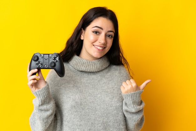 La donna che gioca con un controller per videogiochi è fissata sulla parete gialla che punta di lato per presentare un prodotto