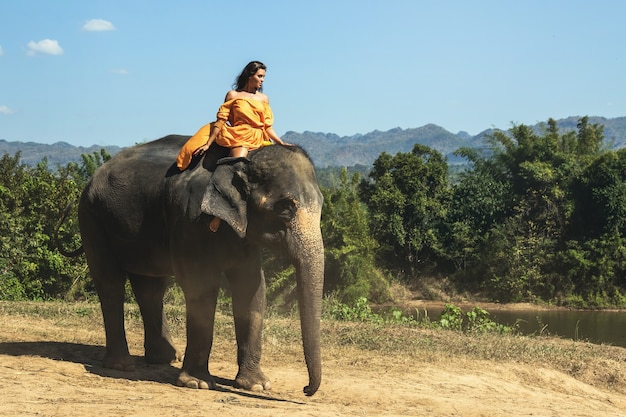 La donna che indossa un bellissimo vestito arancione sta cavalcando il potente elefante