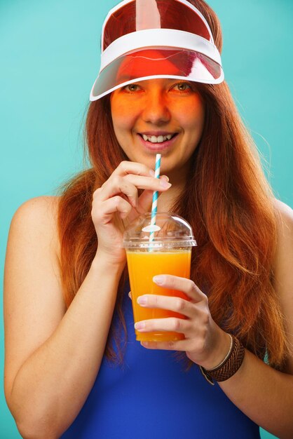 La donna che indossa un costume da bagno blu e un cappello beve il succo di frutta da una tazza