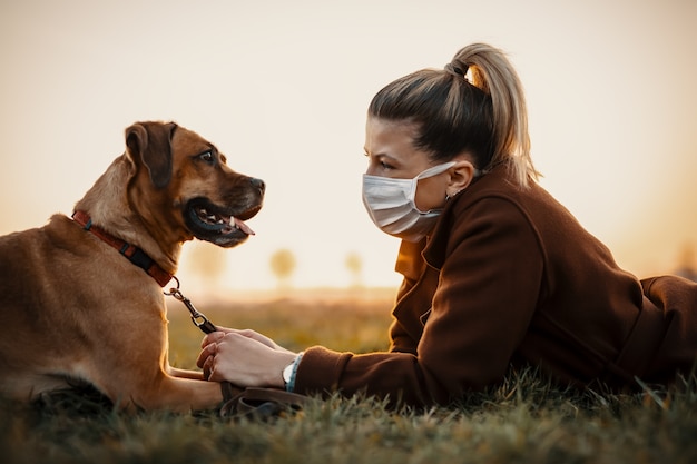 La donna che indossa una maschera cammina da sola con un cane all'aperto a causa della quarantena della corona