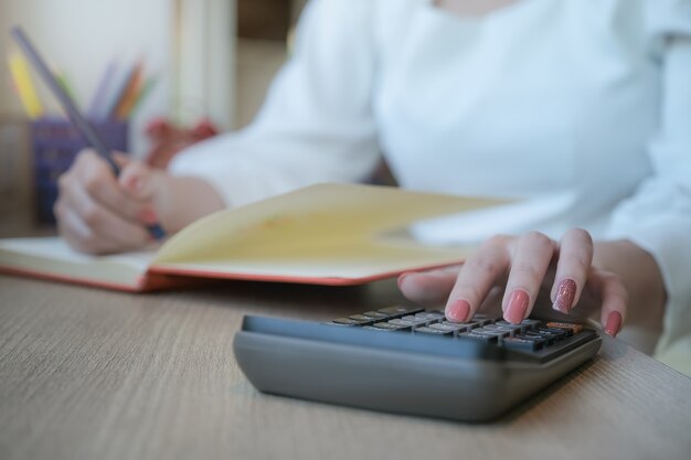 La donna che lavora con le finanze calcola sul calcolatore e che utilizza il taccuino nella stanza dell'ufficio.