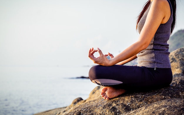 La donna che medita in una posa di yoga sulla spiaggia tropicale.