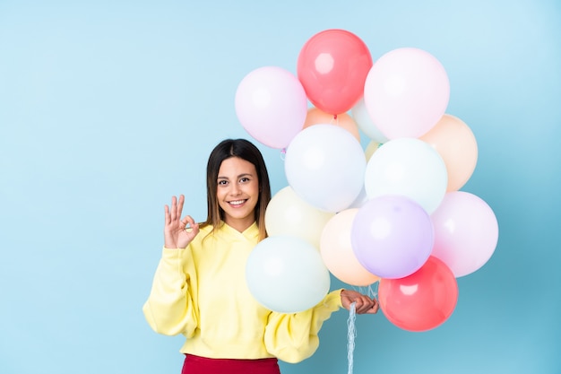 La donna che tiene i palloncini in una festa sul muro blu che mostra un segno ok con le dita