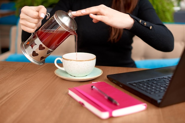 La donna che tiene la teiera nelle mani e l'impiegato o lo studente della tazza si siedono con il computer portatile al tavolo nella caffetteria