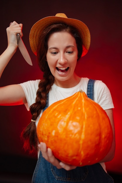 La donna che urla su uno sfondo rosso taglia una lanterna da una zucca con un coltello per halloween