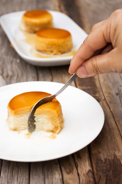 La donna che usando il cucchiaio ha tagliato il dolce casalingo della crema del caramello sul piatto bianco