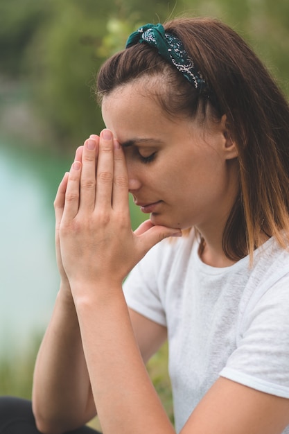 La donna chiuse gli occhi, pregando all'aperto. Mani giunte nel concetto di preghiera per fede, spiritualità e religione