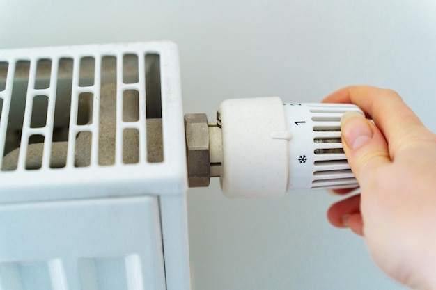 La donna commuta a mano il regolatore di riscaldamento del radiatore al minimo per risparmiare energia termica