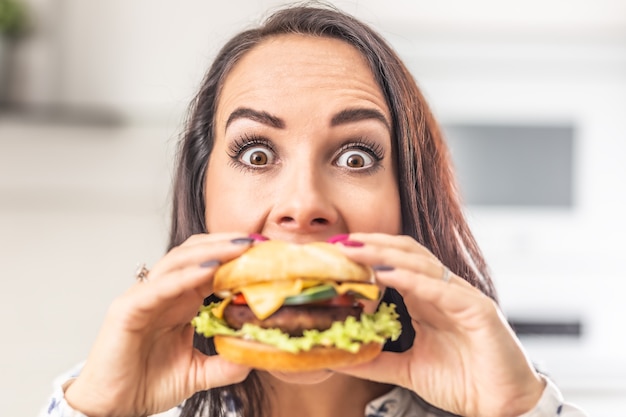 La donna con gli occhi spalancati cerca di addentare un grosso hamburger succoso.