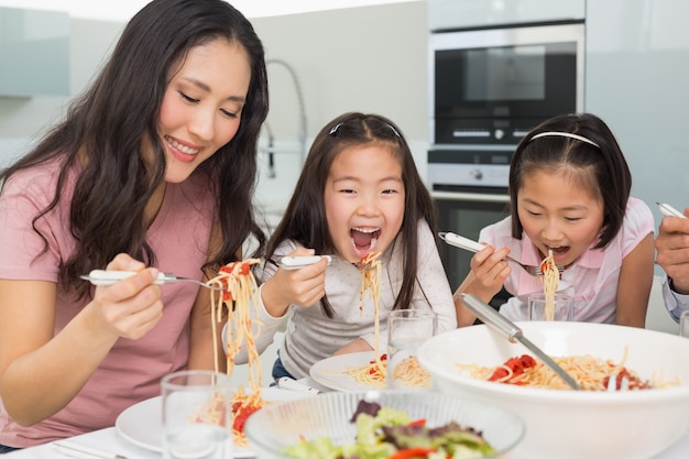 La donna con i bambini che godono degli spaghetti pranza in cucina