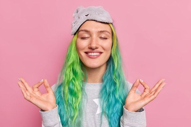 la donna con i capelli colorati tinti tiene gli occhi chiusi fa il gesto mudra si rilassa dopo lo studio o il lavoro medita prima di dormire indossa la biancheria da notte posa sul rosa