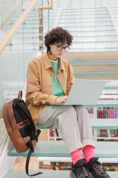 La donna con i capelli ricci è seduta sui gradini e lavora al computer portatile Studentessa spagnola
