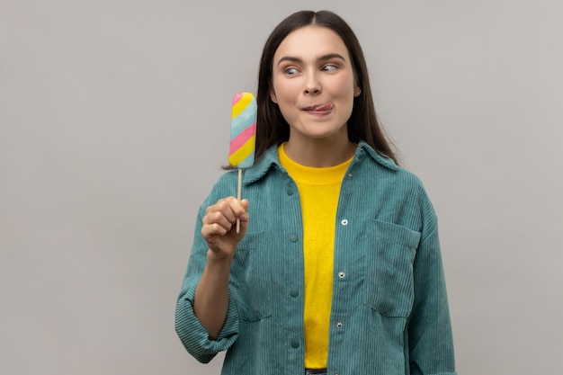 La donna con i capelli scuri che tiene in mano il gelato multicolore si sente affamata e vuole assaggiare il dessert