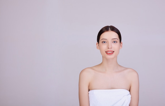 la donna con i capelli scuri in un asciugamano bianco guarda nella cornice, sorride teneramente.