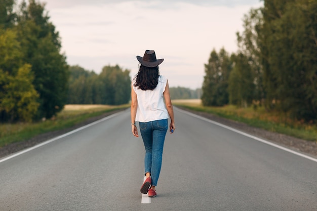La donna con il cappello che cammina sulla strada ha vestito i jeans.