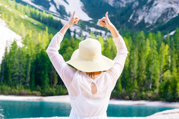 La donna con il cappello di paglia e il vestito bianco mostra il segno come sullo sfondo della foresta di montagne e