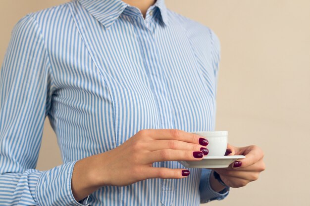La donna con il manicure rosso e la camicia blu che tengono una tazza di caffè si chiudono su