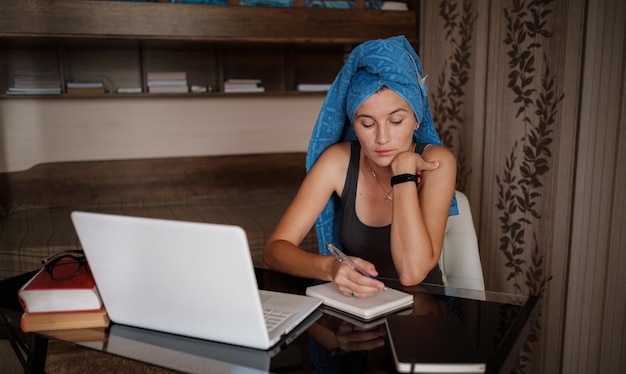 La donna con l'asciugamano blu sulla testa sta lavorando in ufficio a distanza da casa Utilizzando il computer