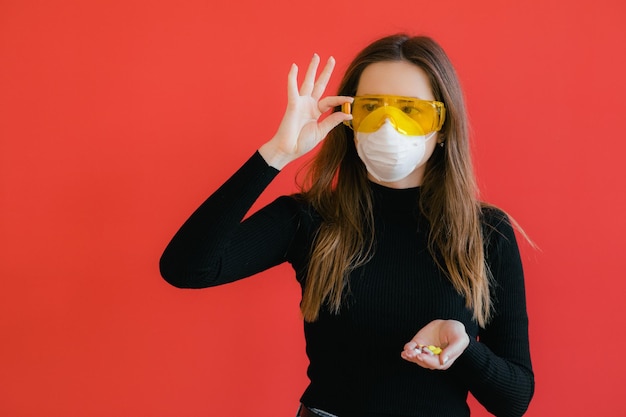 La donna con la maschera protettiva tiene in mano la pillola medica su sfondo rosso