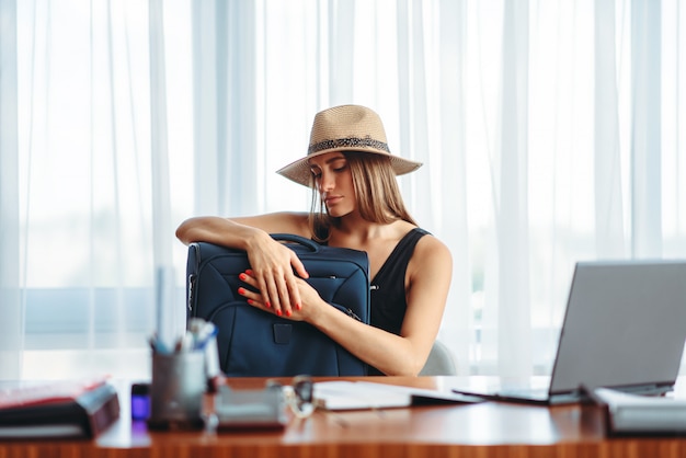 La donna con la valigia al tavolo in ufficio sogna il viaggio.