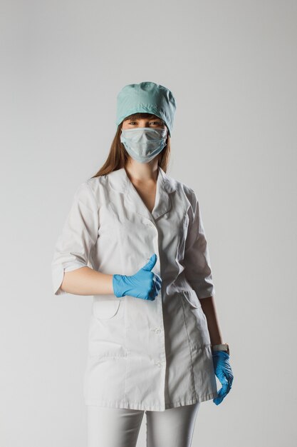 La donna con una maschera medica e le mani in un guanto di lattice mostra il pollice in su. Adoro il nostro medico professionista