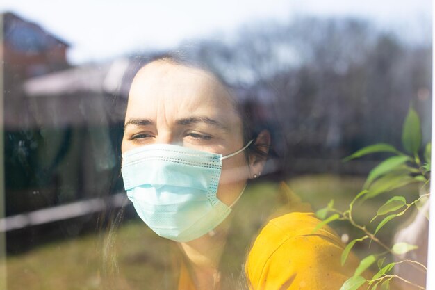 La donna con una maschera medica guarda attraverso la finestra