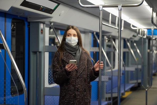 La donna con una maschera medica per evitare la diffusione del coronavirus è in piedi e tiene in mano uno smartphone