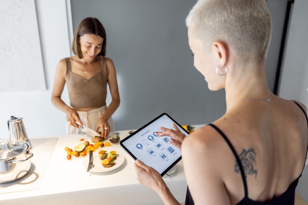 La donna controlla gli elettrodomestici da cucina intelligenti con il dispositivo mobile