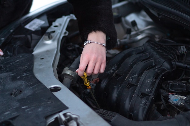 La donna controlla il livello dell'olio nell'auto Preparando l'auto per le condizioni invernali