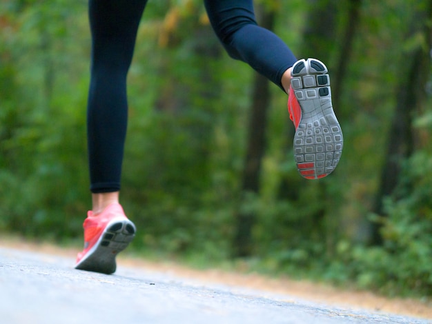 La donna corre nella foresta. Piedi di un corridore. Primo piano di scarpe da ginnastica.