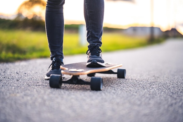 La donna corre su strada dritta sul longboard al tramonto Skater in abbigliamento casual si allena a bordo durante il tramonto serale con luce arancione Ragazza tiene il longboard nelle mani