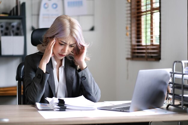 La donna d'affari asiatica è seria sul lavoro causando mal di testa stressato con documenti con un laptop in ufficio