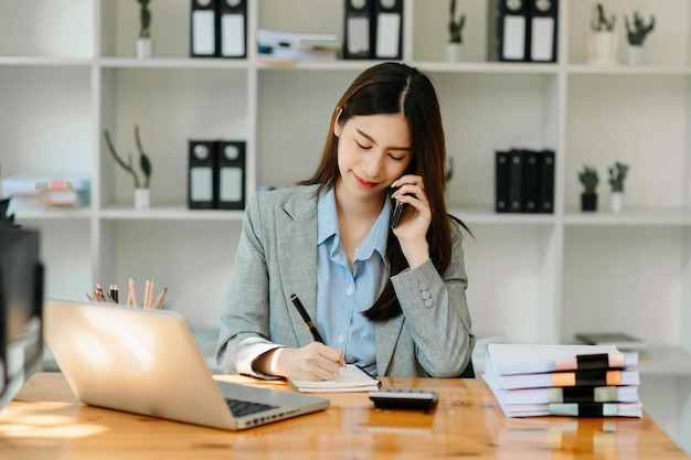 La donna d'affari asiatica ha la gioia di parlare sul tablet smartphone e sul laptop dell'ufficio moderno xA