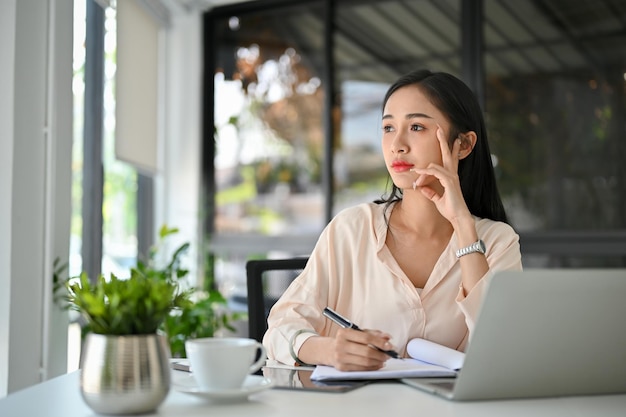 La donna d'affari asiatica millenaria premurosa sta guardando fuori dalla finestra meditando