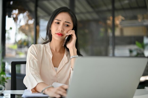 La donna d'affari asiatica millenaria stressata e confusa è al telefono con una telefonata seria