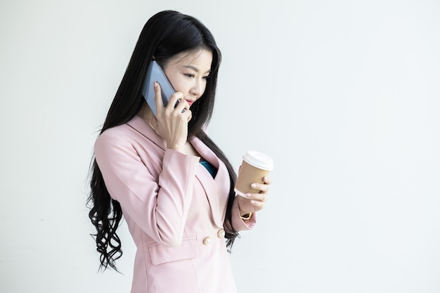 La donna d'affari asiatica sorride e usa lo smartphone e tiene una tazza di caffè Finanza aziendale e occupazione Imprenditrici di successo Donna d'affari sorridente che tiene il caffè utilizzando lo smartphone mobile