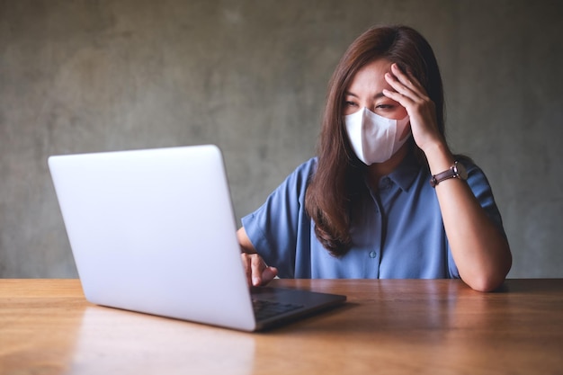 La donna d'affari con la maschera protettiva si stressa mentre lavora su un computer portatile in ufficio