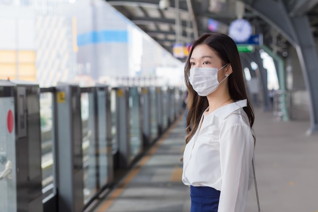 La donna d'affari professionale asiatica con i capelli lunghi indossa la maschera è in attesa di andare al lavoro o in ufficio