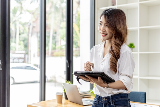 La donna d'affari sta utilizzando un tablet per cercare informazioni e chattare, è titolare di un'azienda, dirige i dipendenti tramite un tablet messenger. Concetto asiatico della donna di affari e uso della tecnologia.