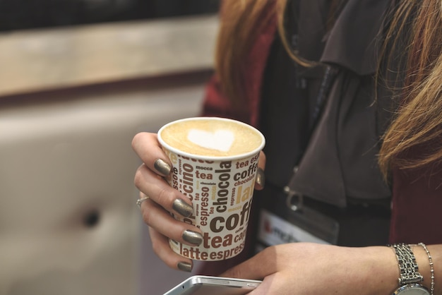 La donna d'affari tiene in mano una tazza di cappuccino con il cuore durante una riunione di lavoro a tono ridotto