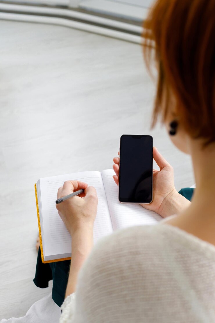 La donna d'affari tiene lo smartphone e fa le annotazioni nel diario