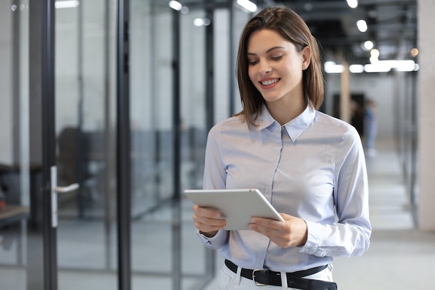 La donna d'affari usa la tavoletta digitale in piedi nel corridoio dell'ufficio.