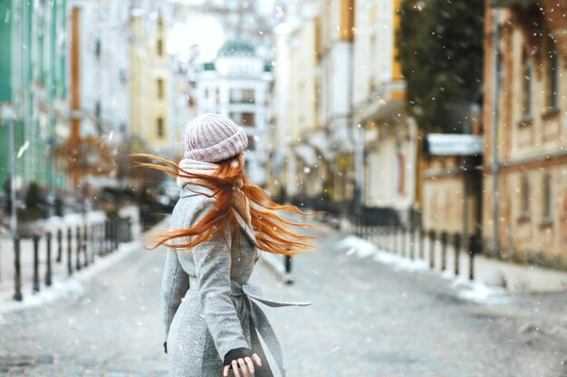 La donna dai capelli lunghi allo zenzero soddisfatta indossa un cappotto elegante che cammina per strada durante le vacanze di Natale con la neve. Spazio per il testo